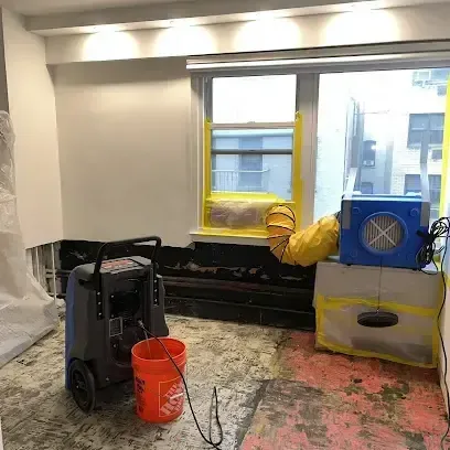 A dehumidifier and an air mover drying an emptied room after the flooring was pulled up during a dry-out