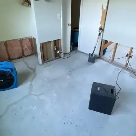 Air movers and a dehumidifier drying a room with its lower drywall cut out and bare floor