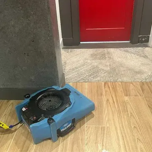 An air mover pushing air across a wood-look tile floor beside an open doorway