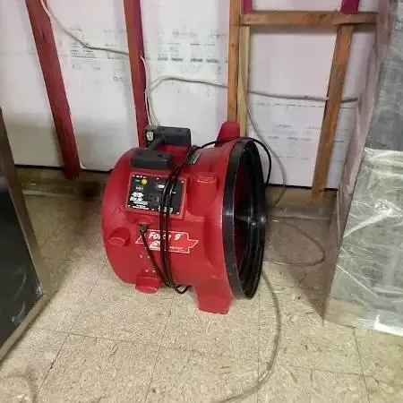 Red air mover drying a room with the lower wall opened and plastic sheeting hung after a leak