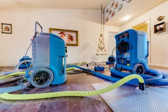 Air movers and a dehumidifier aimed at wet walls inside a home