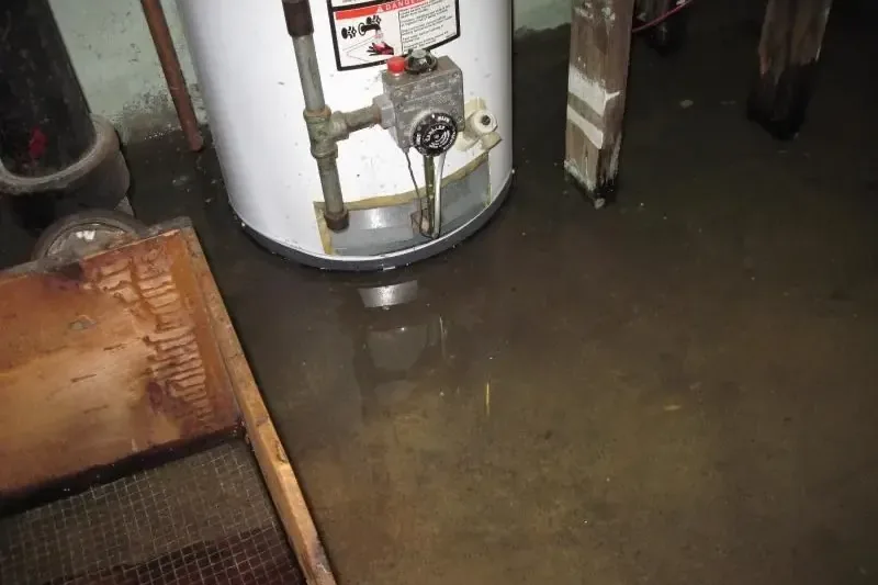 A leaking water heater sitting in a puddle on a utility room floor